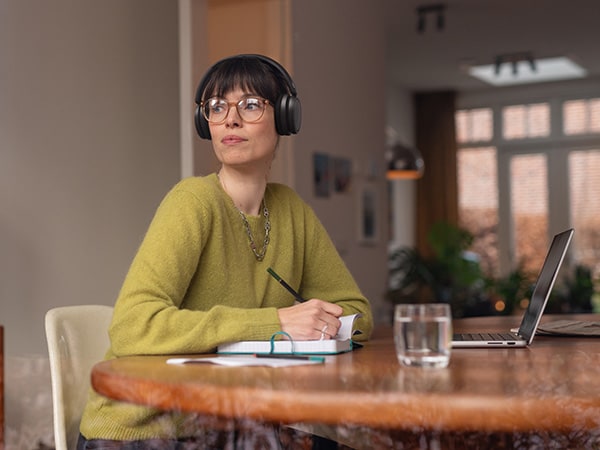 Людина в зручних навушниках Philips сидить за столом з блокнотом і ноутбуком.