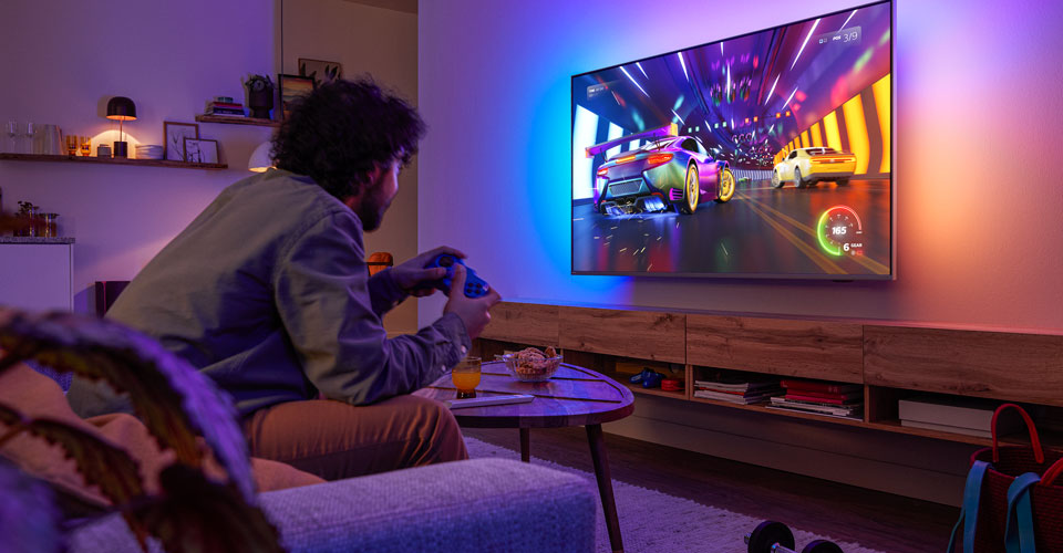 Людина сидить на дивані й грає в гоночну відеогру на телевізорі Philips Ambilight.