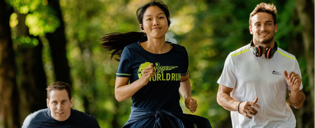 Троє учасників марафону Wings for Life World Run зі спортивними навушниками Philips радісно біжать.