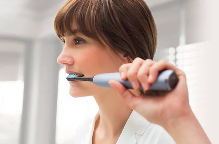 Жінка чистить зуби електричною зубною щіткою Philips Sonicare.
